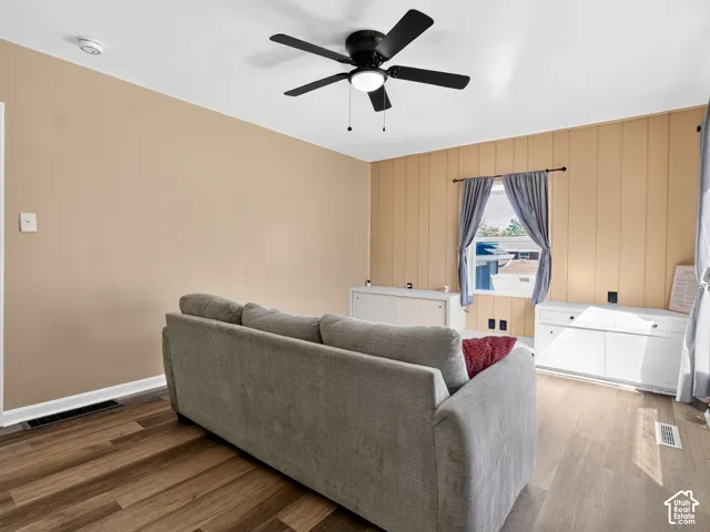 Wood-finish flooring, vertical panel wall detailing, and a black ceiling fan with an integrated light fixture