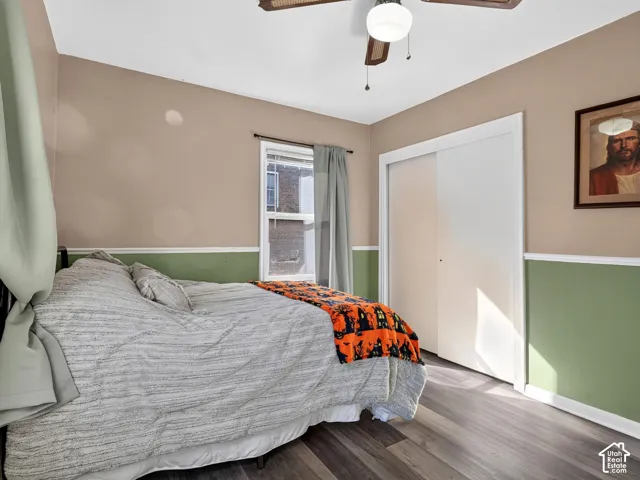 Wood-finish flooring, dual-tone walls with wainscoting, sliding-door closet, and a ceiling fan with light fixture