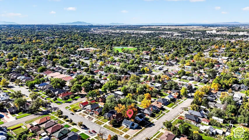 Aerial perspective of a detached residential property situated on a corner lot, featuring mature trees and a grid-patterned street layout