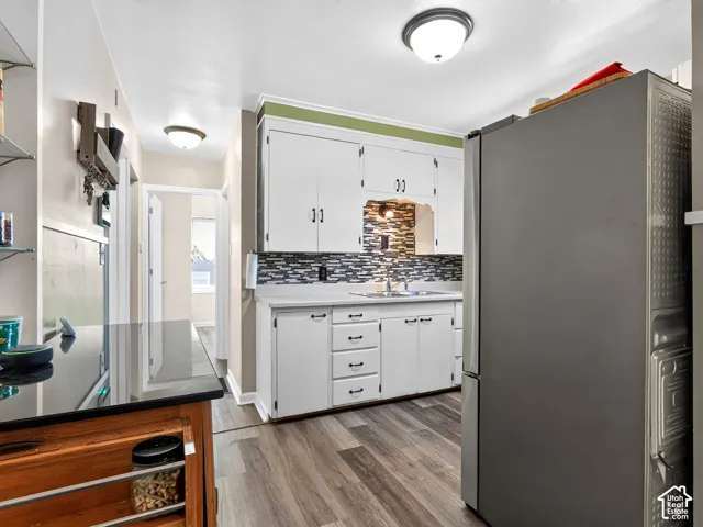 Kitchen featuring white cabinetry, wood-finish flooring, a stainless steel refrigerator, stone-tiled backsplash, and a black countertop surface