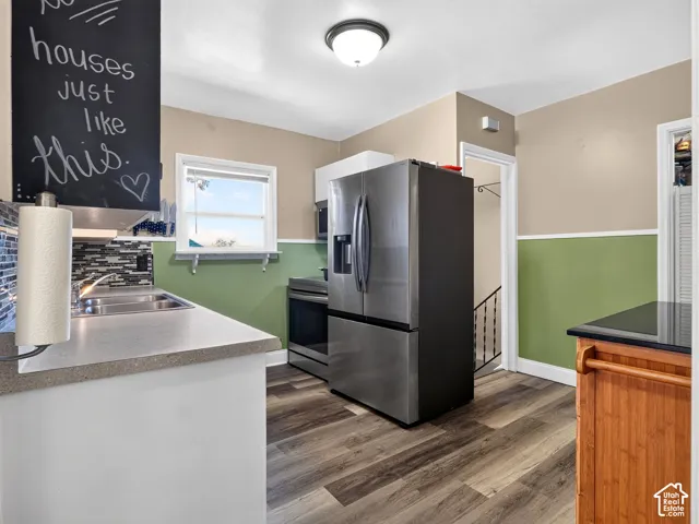 Kitchen featuring stainless steel appliances, wood-finish flooring, multi-colored glass tile backsplash, and neutral-toned wall paint