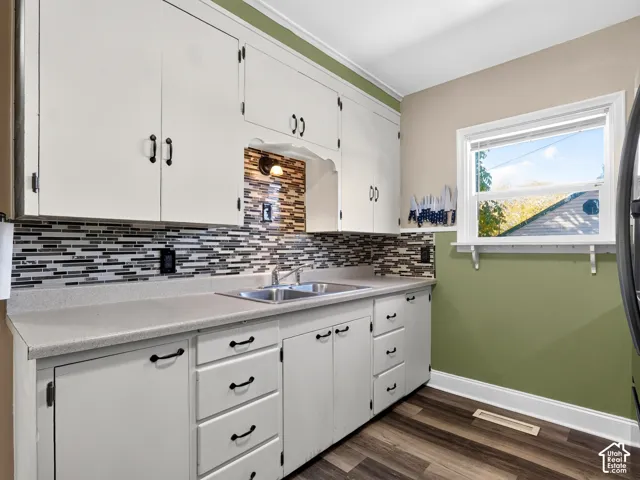 Kitchen featuring white cabinetry with matte black hardware, dual-basin stainless steel sink, multi-tone glass tile backsplash, and wood-finish flooring