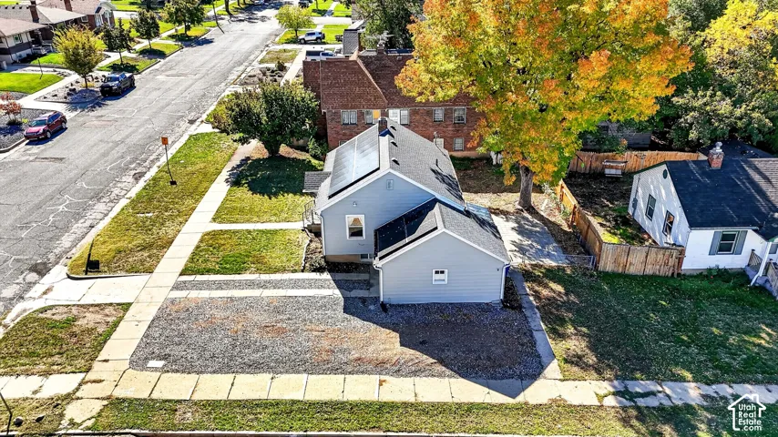 Exterior featuring grey vinyl siding, roof-mounted solar panels, asphalt shingle roof, gravel driveway, and mature landscaping