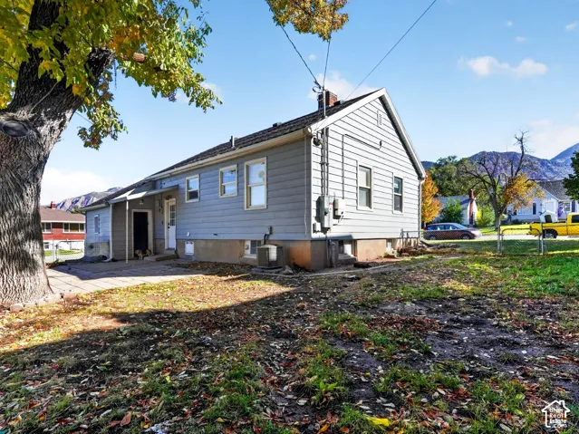 Exterior features include horizontal siding, a concrete patio, and a mature tree situated on a lot with mountain scenery