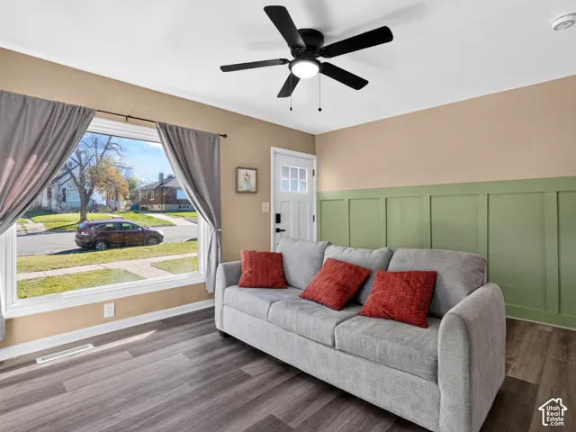 Room featuring wood-finish flooring, sage green board-and-batten wall paneling, a multi-pane glass entry door, and a black ceiling fan with integrated lighting