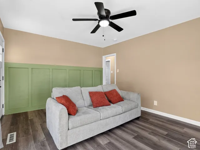 Room featuring green wall paneling, wood-finish flooring, and a ceiling-mounted light fixture with a five-blade fan