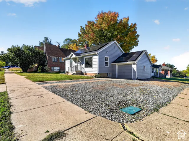 Single-story residence featuring light-colored horizontal siding, a front-facing gable roof, integrated solar panels, an attached garage, and a gravel driveway