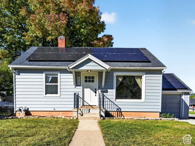 Single-story residence featuring light blue siding, solar panels, a gable roof entrance, and an attached garage