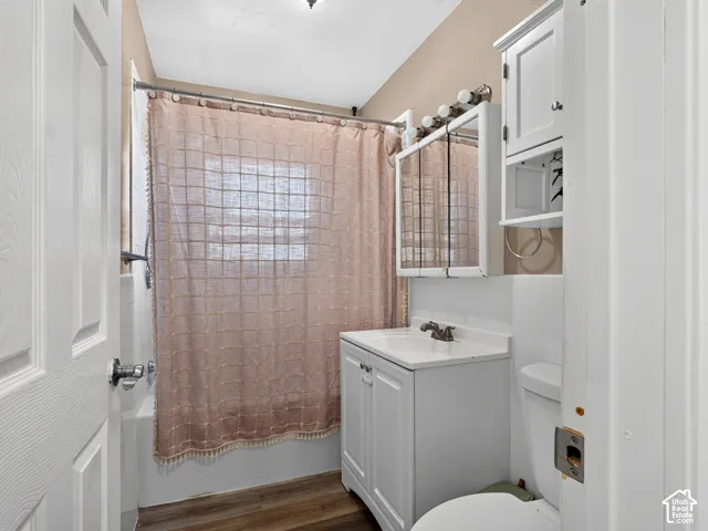 White vanity with integrated sink, tri-fold mirrored medicine cabinet, overhead light fixture, wood-finish flooring, and built-in wall cabinetry
