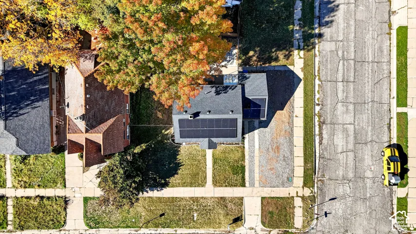 Aerial view of a residential property featuring an asphalt shingle roof equipped with solar panels, a paved driveway, and mature landscaping