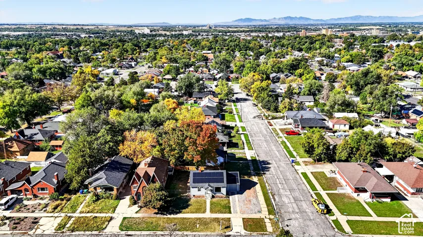 Aerial perspective featuring solar panel installation, mature deciduous trees, and distant mountain scenery