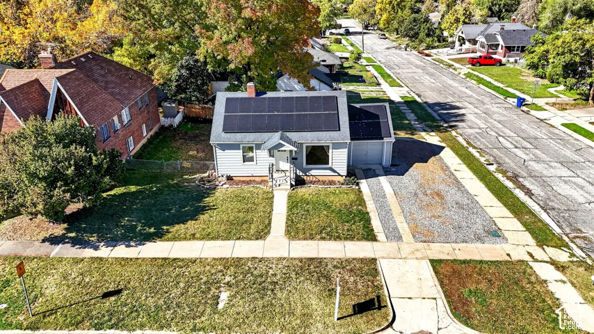 Single-story residence featuring a shingled roof with installed solar panels, front-facing chimney, attached single-car garage, and a gravel driveway