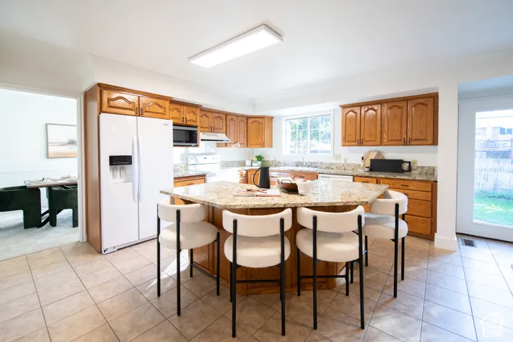 Kitchen featuring an expansive center island, stone-finish countertops, wood-finish cabinetry, tile flooring, and a glass-paneled exterior door