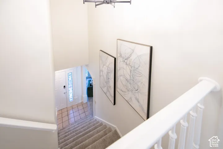 Entryway featuring high ceilings, a staircase with carpeted steps, a white wooden balustrade, and a front door with a vertical decorative glass inlay