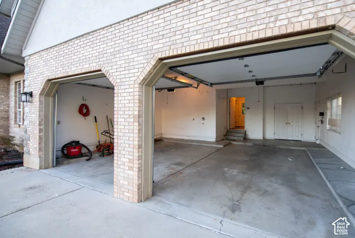 Three-car garage featuring a brick exterior facade, concrete flooring, overhead lighting, and double-door interior entry
