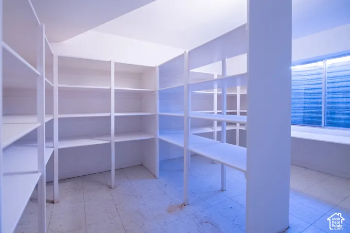 Walk-in storage space featuring extensive white built-in shelving, tile flooring, and a single-pane horizontal window