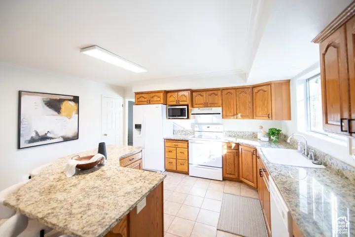 Kitchen featuring stone-finish countertops, natural wood cabinetry, a white under-mount sink, tile flooring, and a center island with built-in storage