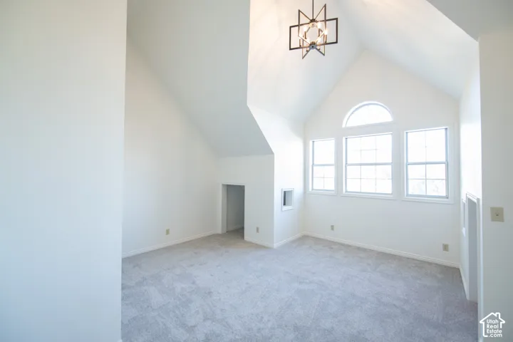 Vaulted ceilings, geometric metal chandelier, arched accent window, multi-pane windows, and neutral carpeting