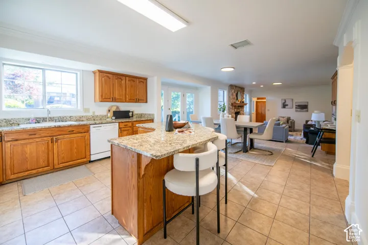 Kitchen featuring stained wood cabinetry, stone-surface countertops, central island, tile flooring, and a stone-faced fireplace