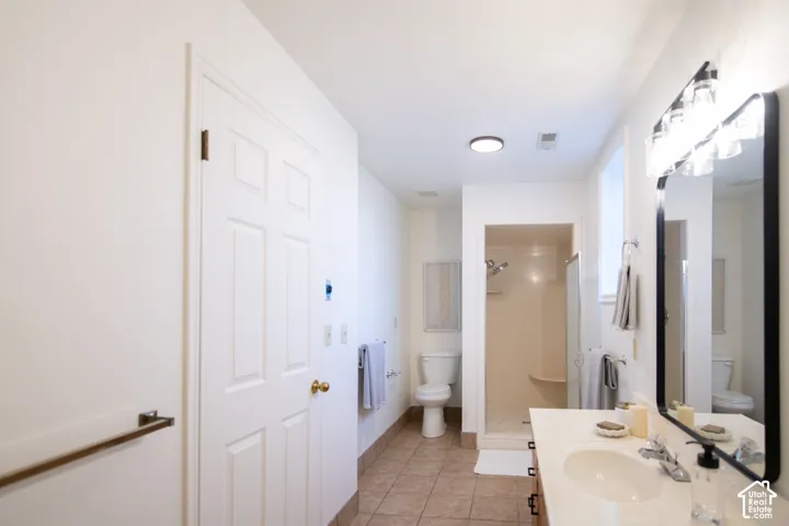 Bathroom featuring tile flooring, a vanity with an integrated sink, a rectangular mirror with a black frame, multi-bulb wall lighting, and a walk-in shower enclosure