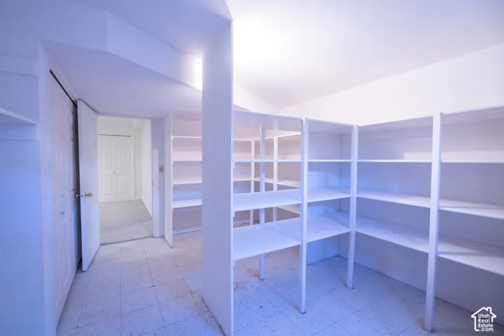 Storage space featuring floor-to-ceiling built-in white shelving, tiled flooring, and a multi-panel door