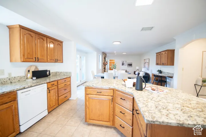Kitchen featuring solid wood cabinetry, expansive stone countertops, a large center island, and neutral tile flooring