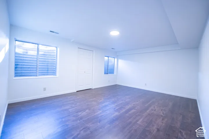 Interior space featuring wood-finish flooring, white walls, flush-mount lighting, two egress windows with window wells, and a multi-panel door