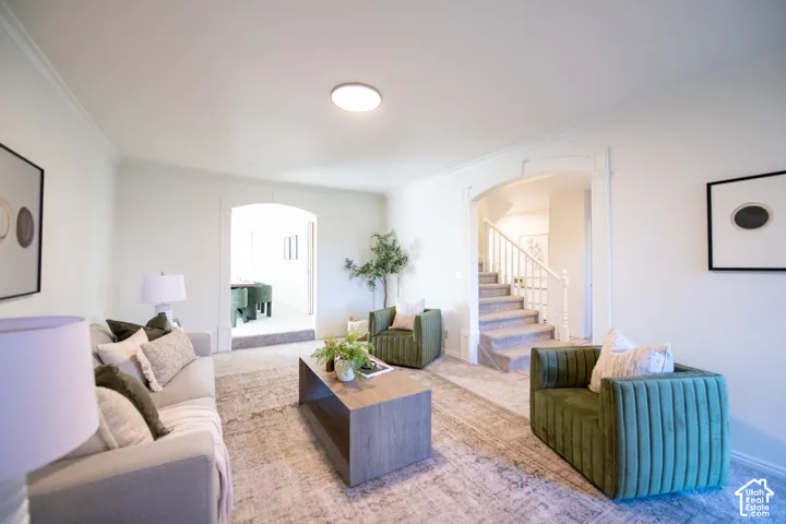 Living area featuring crown molding, two distinct arched pass-throughs, neutral carpeting, and a staircase with a white balustrade