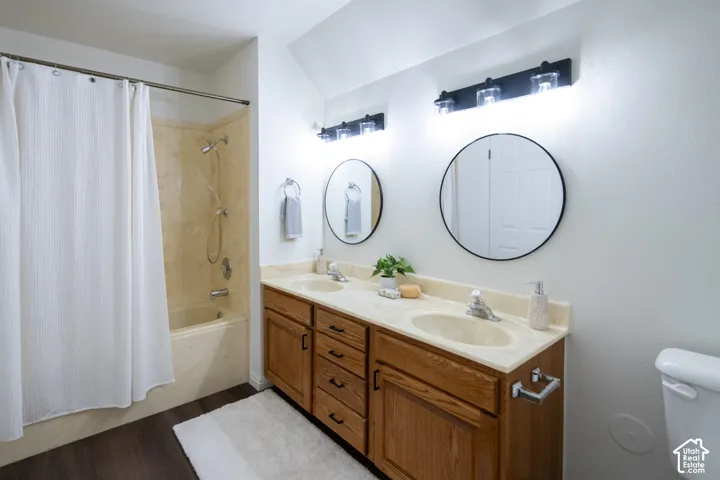 Bathroom featuring a double-sink vanity with wood-finish cabinetry, neutral countertop, dual round wall-mounted mirrors, and a combination tub-shower with solid-surface surround