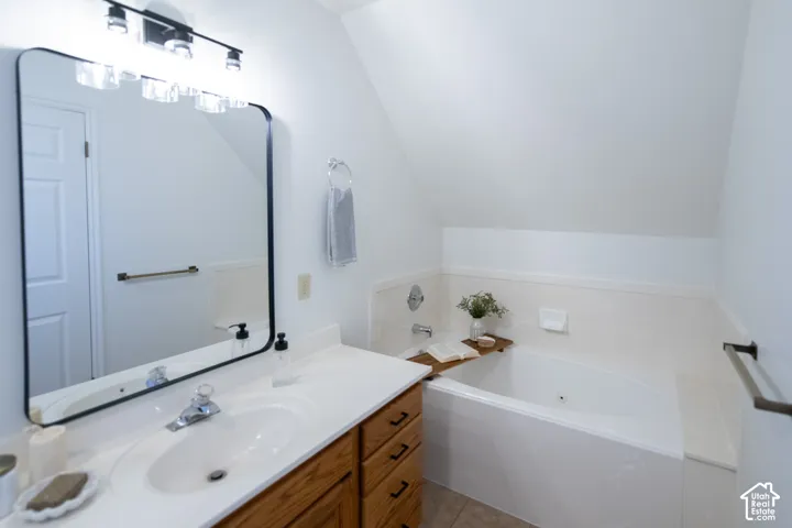 Bathroom featuring an oval jetted tub with integrated tile surround, wood-finish cabinetry, a white countertop with an inset basin, and a wall-mounted vanity mirror with a black frame