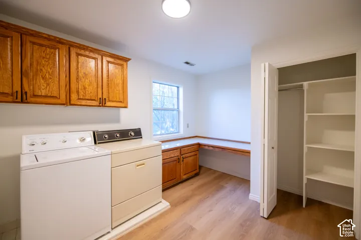 Laundry room featuring wood-finish flooring, wood cabinetry, a built-in folding counter, and a walk-in closet with built-in shelving