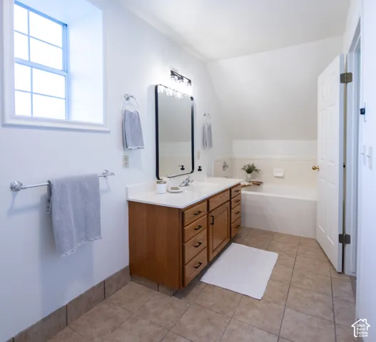 Bathroom featuring tile flooring, a wood-finish vanity with a white countertop, a recessed bathtub with tile surround, and a rectangular mirror with a black frame