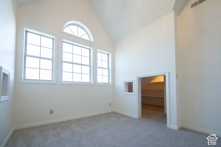 Vaulted ceiling, multi-pane windows with an arched transom, neutral wall-to-wall carpeting, and an integrated storage alcove with built-in shelving