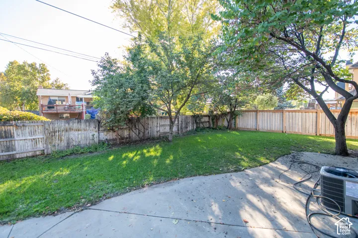 Private backyard featuring a concrete patio, grassy lawn, mature trees, and wooden perimeter fencing