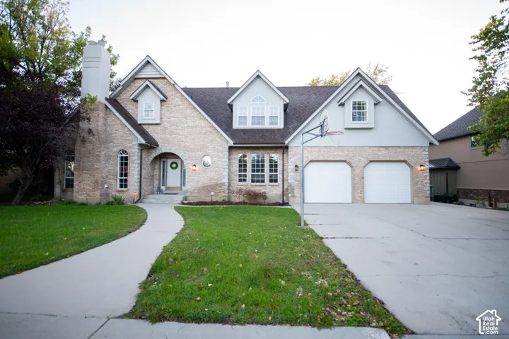 Two-story exterior featuring light-toned brick facade, arched entryway, multiple gabled rooflines, dormer windows, and attached two-car garage