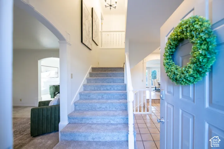 Foyer featuring a light-toned door, ceramic tile flooring, a carpeted staircase with a white balustrade, and arched architectural openings