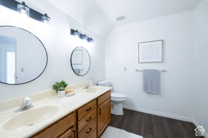 Dual-vanity cabinetry with an integrated countertop and dual basins, two circular wall-mounted mirrors, dark wood-finish flooring, and industrial-style multi-light fixtures
