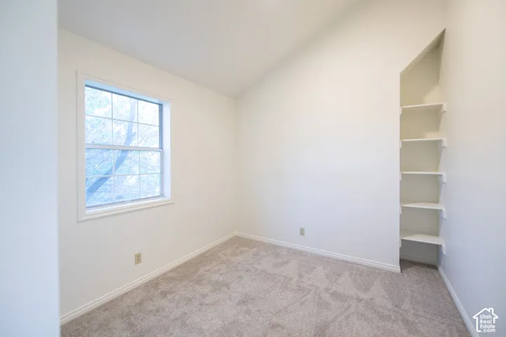 Room featuring vaulted ceilings, neutral carpeting, a grid-pattern window, and built-in wall shelving