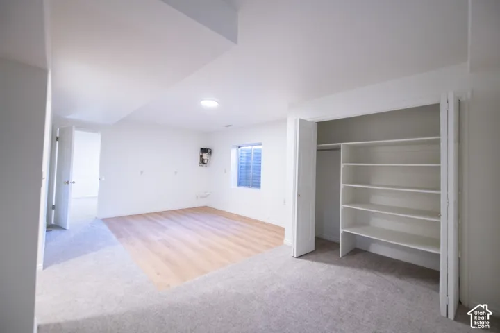 Neutral-toned room featuring a central section of wood-finish flooring, wall-to-wall carpeting, an egress window, and a built-in closet with multi-tier shelving