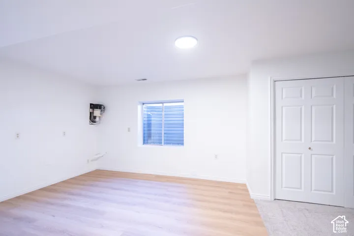 Interior room featuring wood-finish flooring, white walls, a flush-mount ceiling light, a window with a window well, and double-panel doors