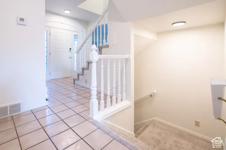 Entryway featuring tile flooring, a white paneled door with sidelights, and a staircase with a white balustrade and carpeted treads