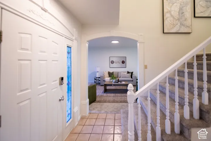 Entryway featuring ceramic tile flooring, an arched doorway with decorative trim, a white door with stained glass sidelight, and a staircase with a white balustrade