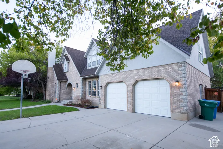 Multi-level exterior featuring light-toned brick masonry, stacked stone quoins, a dual-bay garage, and an asphalt shingle roof