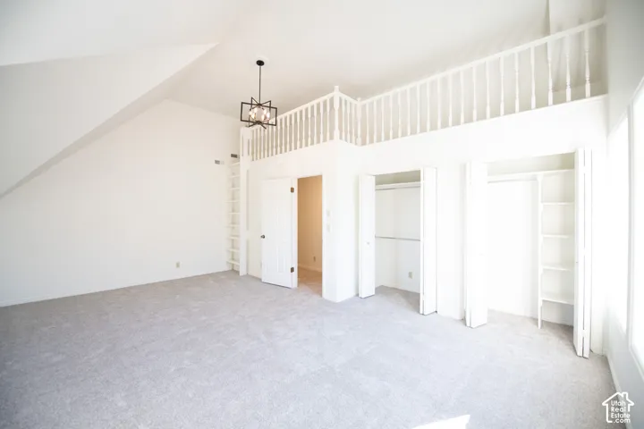 Vaulted ceilings featuring a built-in loft area with a balustrade, integrated ladder access, two reach-in closets with shelving, and a multi-light geometric chandelier