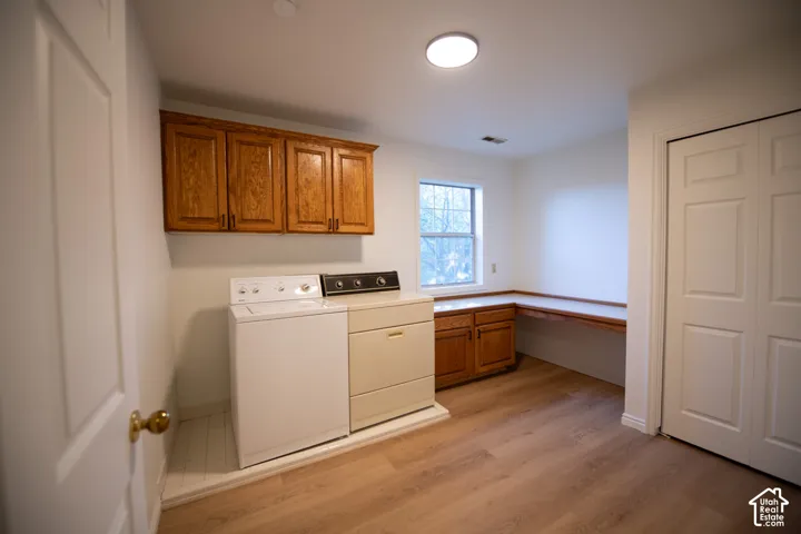 Laundry room featuring wood-finish flooring, upper and lower wood cabinetry, an integrated folding counter, and a recessed window