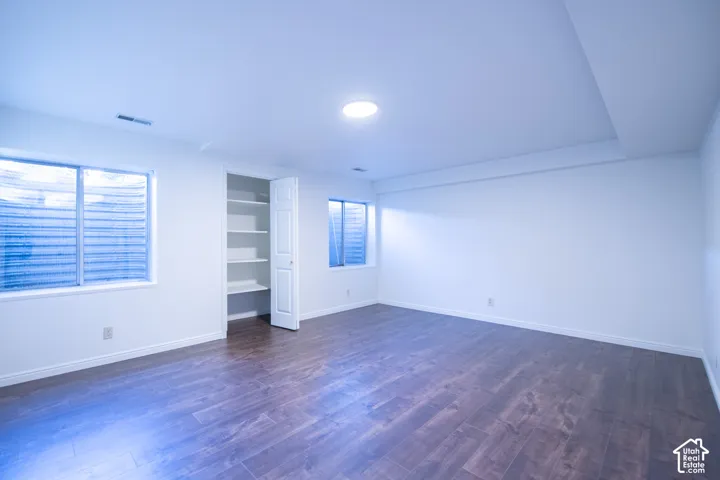 Room featuring wood-finish flooring, white walls, two egress windows with window wells, and a built-in closet with integrated shelving