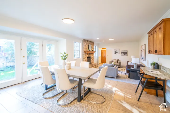 Open-concept area featuring stone-surround fireplace, tile flooring, glass-paned double doors, and built-in cabinetry with natural stone countertop