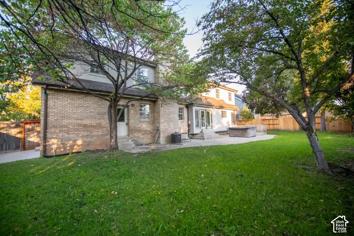 Backyard featuring a brick and composite exterior, expansive lawn, mature trees, hardscape patio, and wood privacy fencing