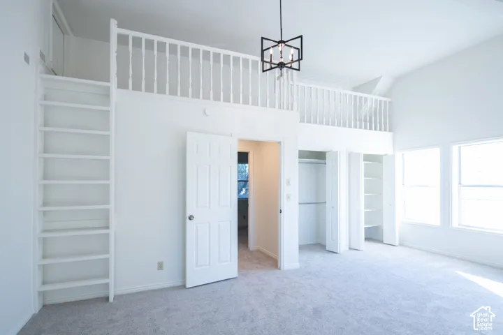 High-ceilinged room featuring a wooden loft area with white railings, a built-in vertical storage ladder, multiple closets with shelving, and a modern black geometric chandelier