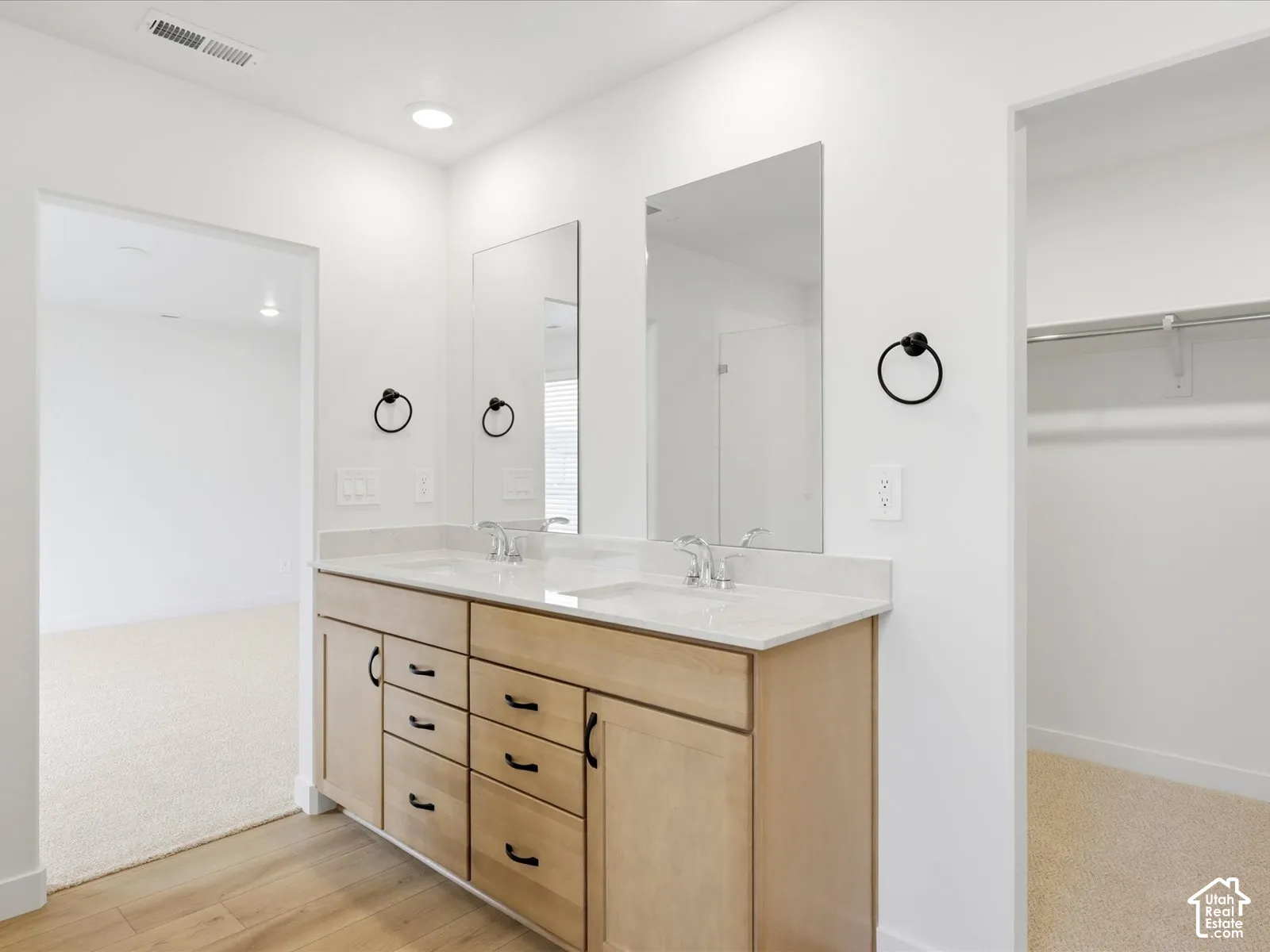 **DISCLAIMER**  Interior package may vary. Dual-sink vanity with light-tone wood cabinetry, stone-composite countertop, matte black hardware, and wall-mounted ring towel holders